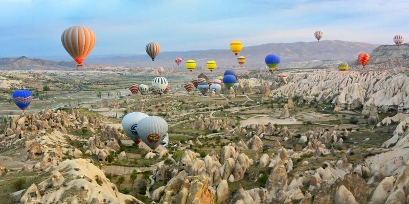 Colorful hot air balloons flying over rocky hills in Cappadocia, a famous place for Indians visiting Turkey with a visa.