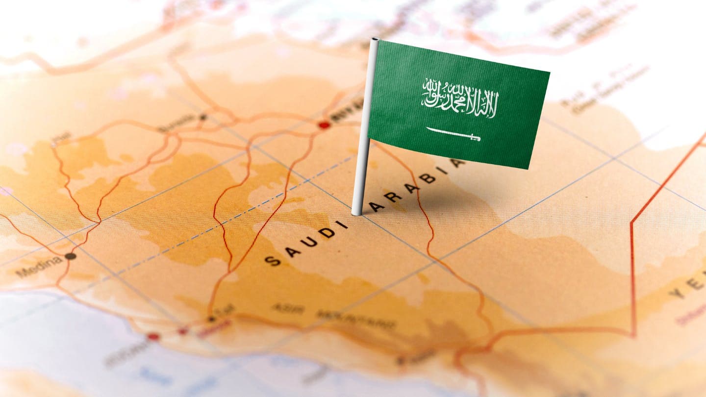 Small Saudi Arabian flag pinned to a detailed map of Saudi Arabia, highlighting its location and key cities.