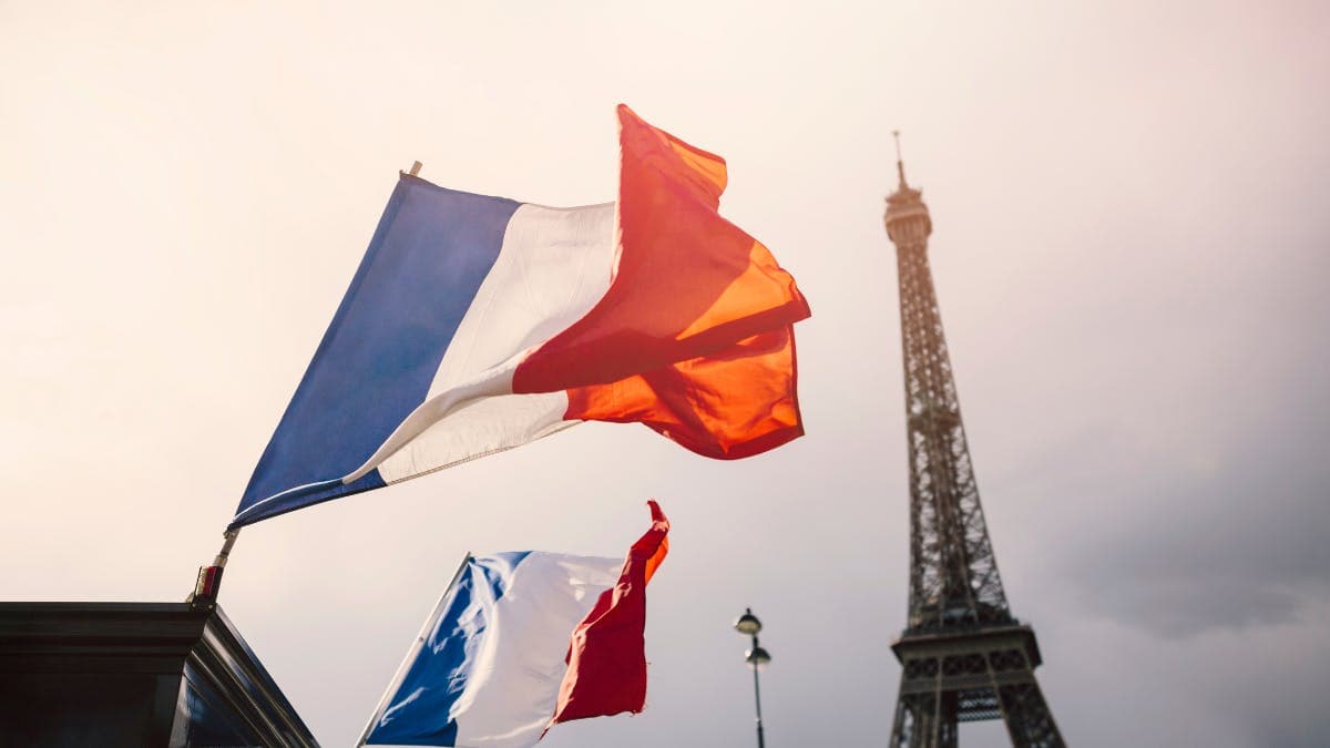 French flags fluttering in the wind with the Eiffel Tower in the background.