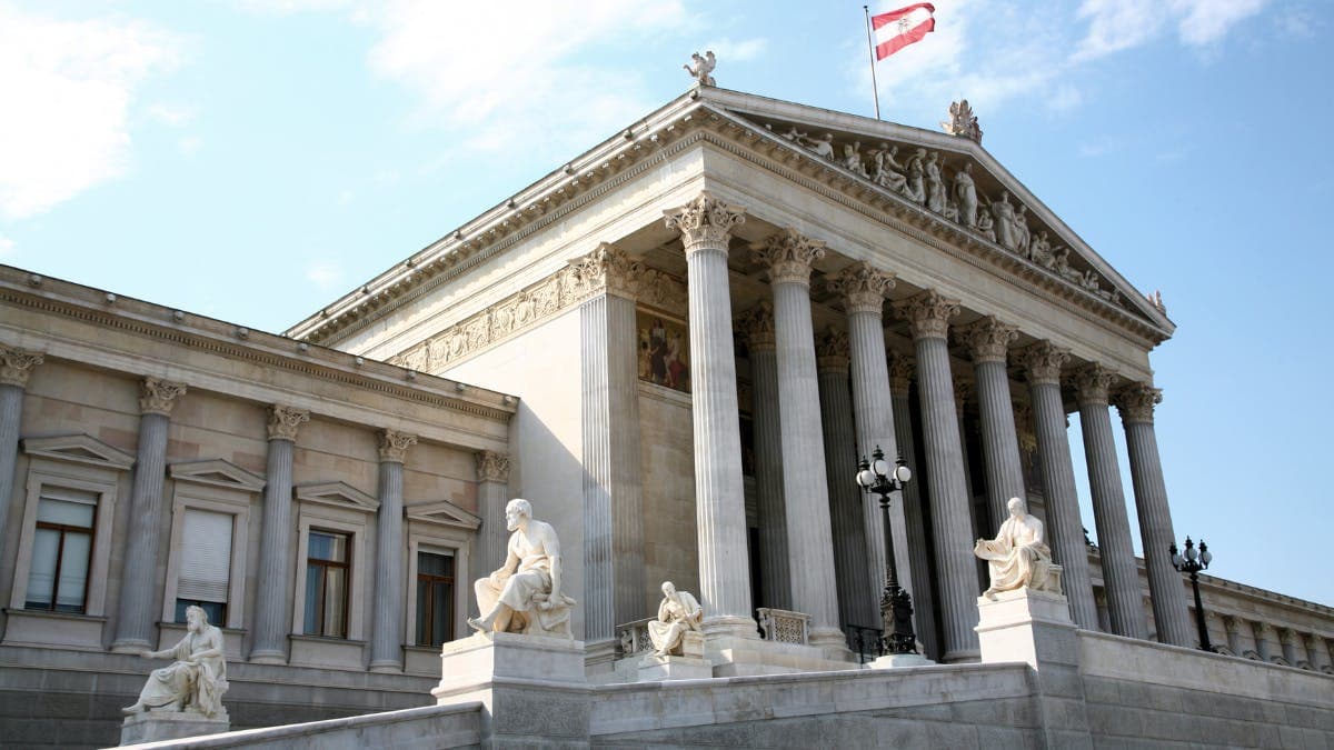 Statues and columns of a neoclassical building with an Austrian flag on top.