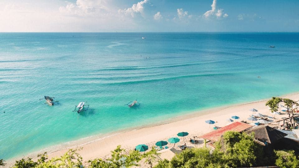 A serene tropical beach in Bali with boats on the turquoise sea.