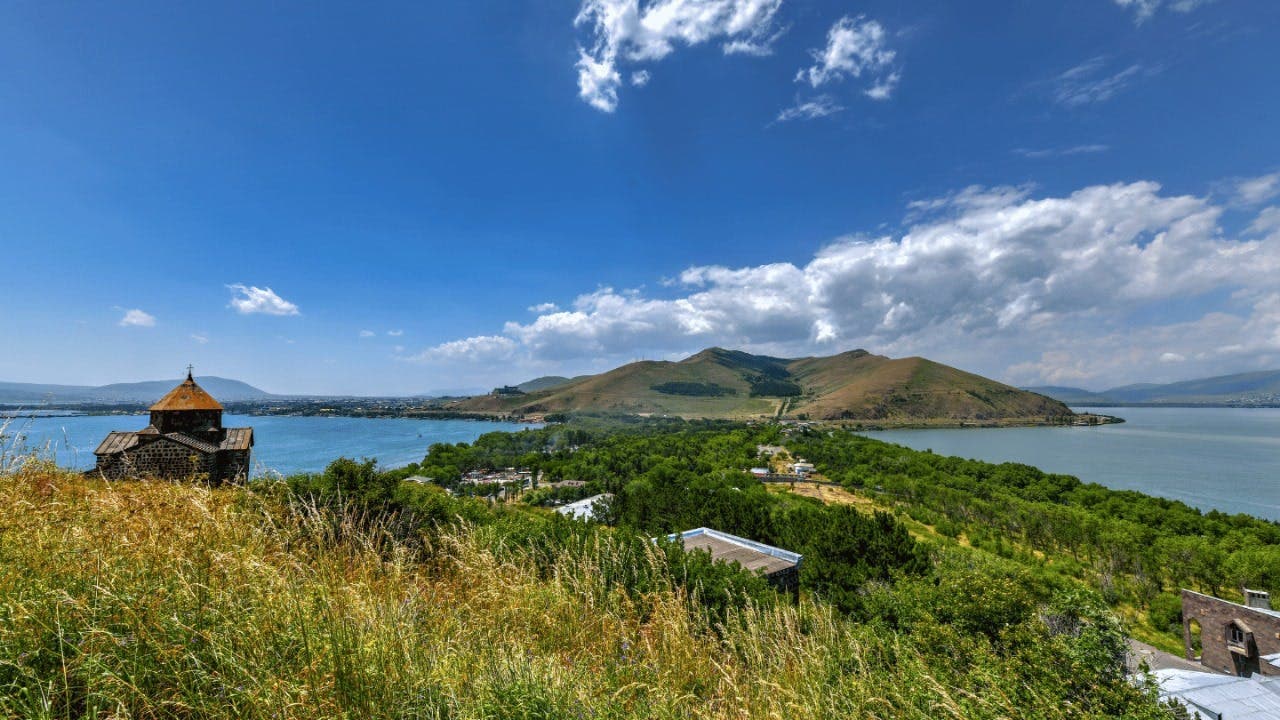 Scenic lake view in Armenia with a historic stone church and green hills.